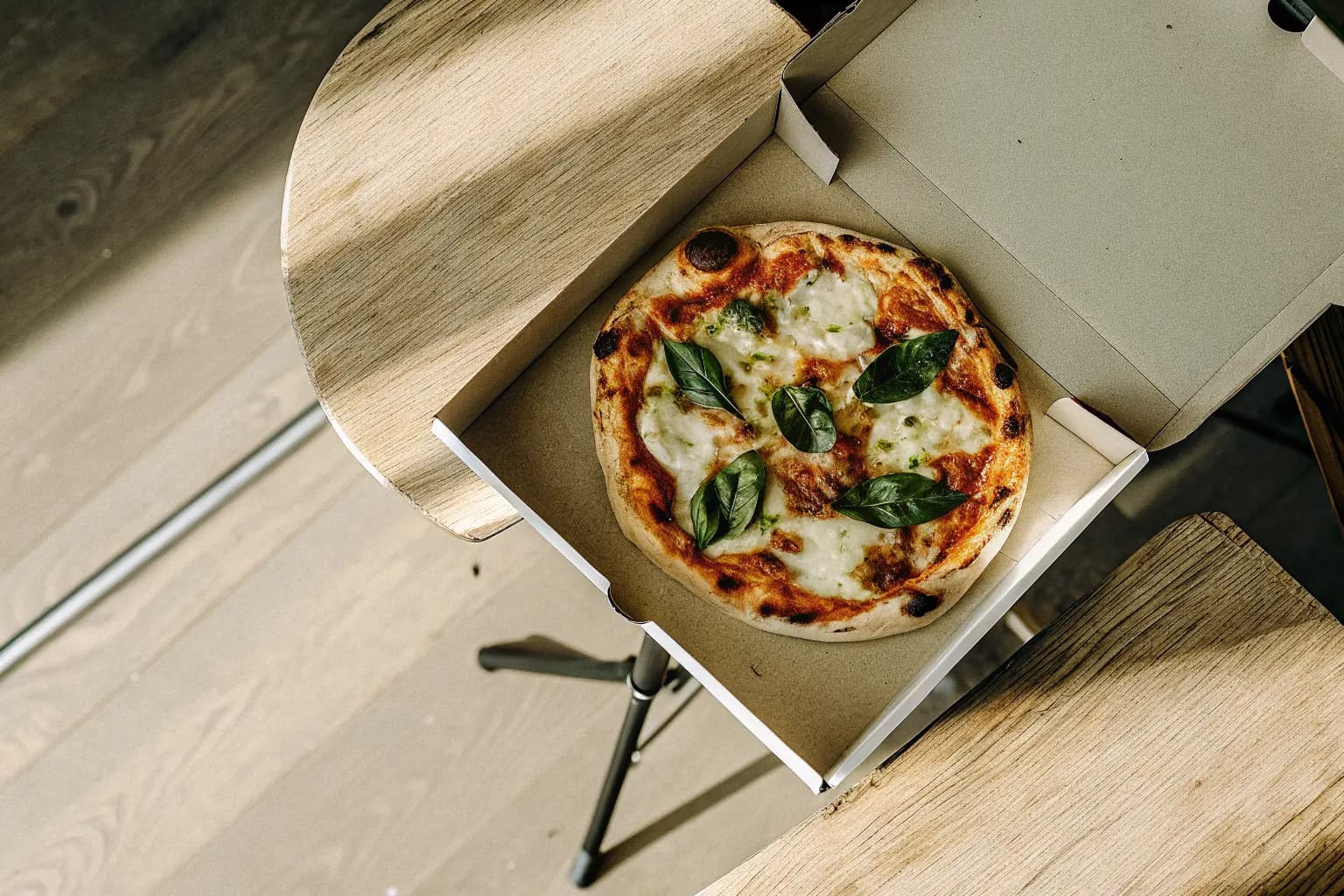 Freshly baked pizza in an open delivery box with a biodegradable PHA pizza saver tripod — sustainable pizza delivery packaging alternative to conventional polystyrene