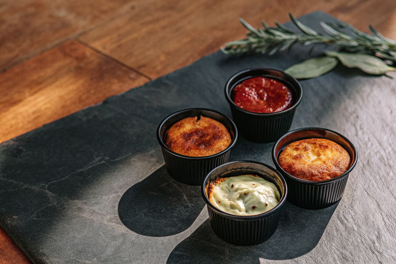 Small black souffle portion cups filled with sauces and dressings on a dark slate surface — sustainable condiment packaging alternative to conventional plastic