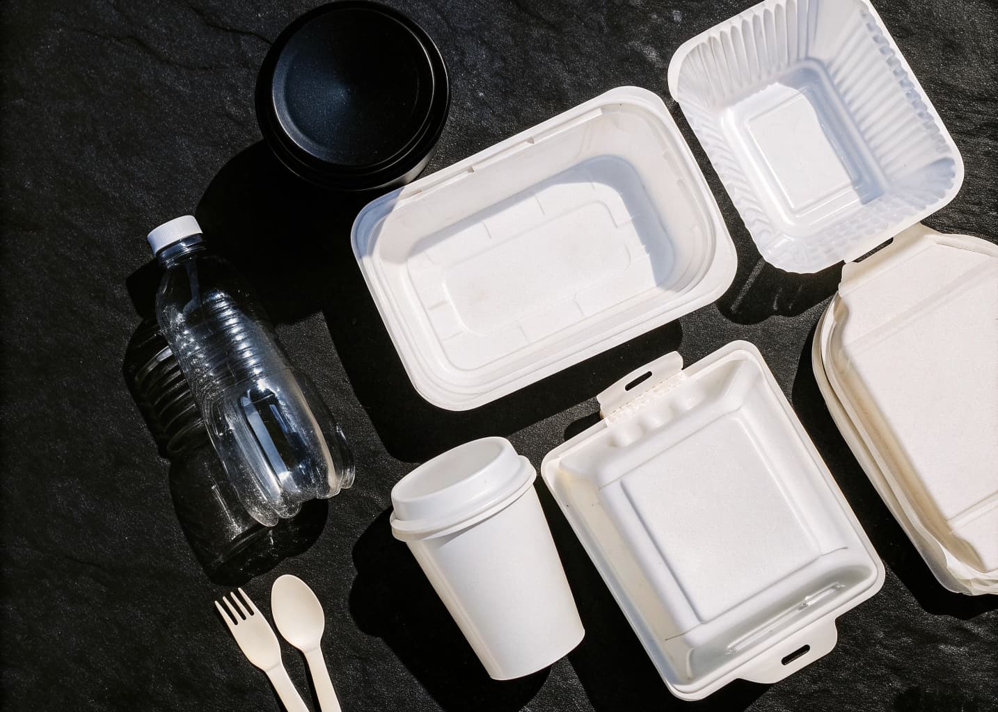 A flat lay of common single-use plastic packaging waste including bottles, containers, cups, and utensils